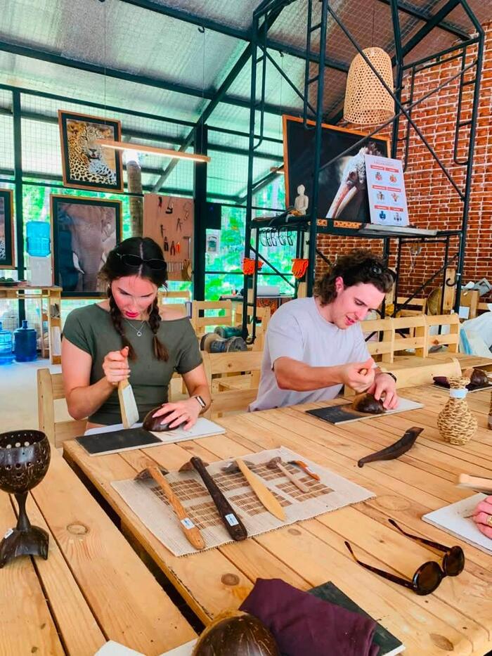 Two visitors shaping coconut shells with hand tools at the workbench.