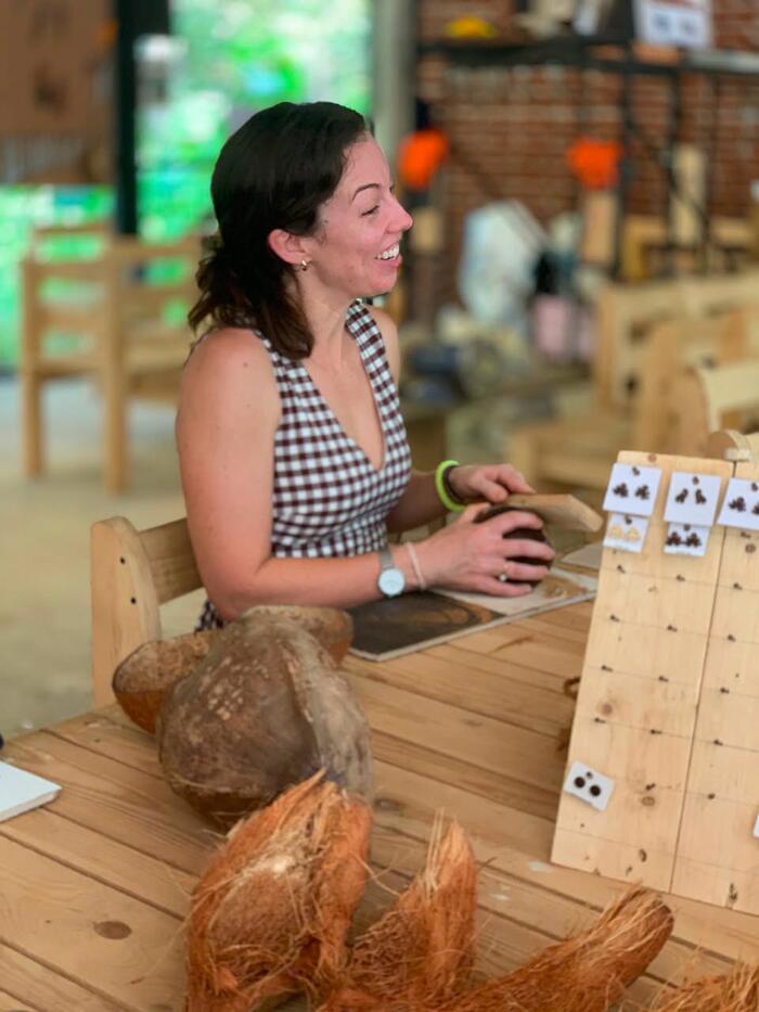 A visitor laughing while working a coconut shell beside a rack of finished earrings.